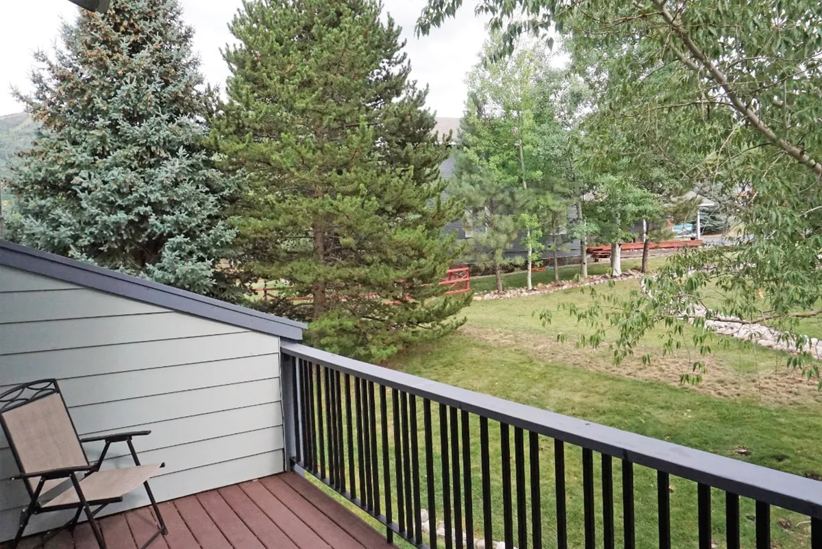 A deck scene with a simple chair, deck railing, and a view of trees and surrounding landscape. The area is calm and peaceful, perfect for relaxing, reading, or enjoying beautiful ski area views. The outdoor setting connects the interior gathering spaces to the natural mountain environment.