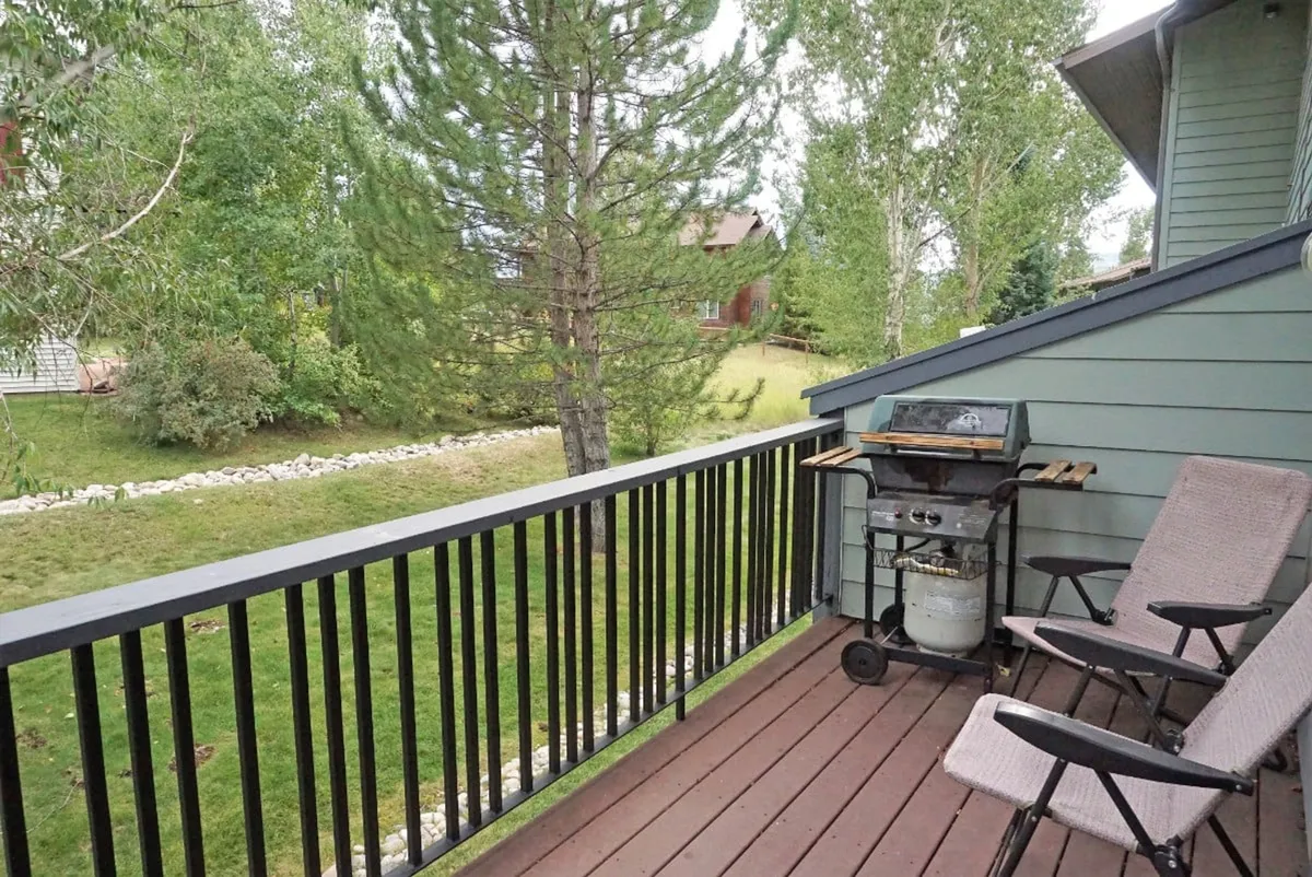 A welcoming deck space equipped with a grill, comfortable deck chairs, and surrounded by mature trees. The setup highlights the opportunity for outdoor relaxation and gatherings, while the natural setting suggests a close relationship with the Yampa River and bike trails.