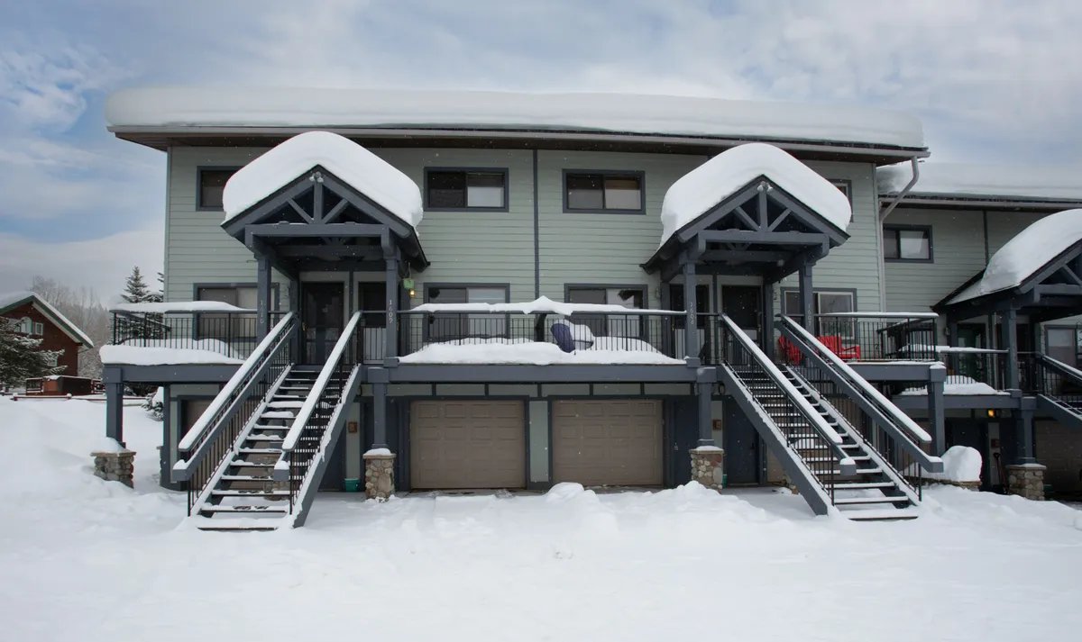 An exterior shot showing snow-covered roofs, staircases, garage doors, and front balconies, evoking the property's mountain environment and providing context for the entry and garage areas.