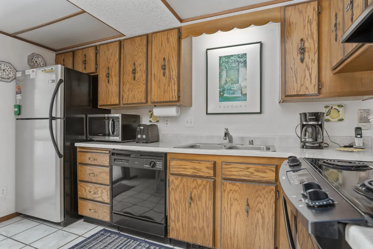 The image highlights a homey kitchen with a refrigerator, dishwasher, sink, stove, and plenty of cabinets. The space looks inviting and practical, with multiple appliances easily accessible for meal preparation and cleanup.