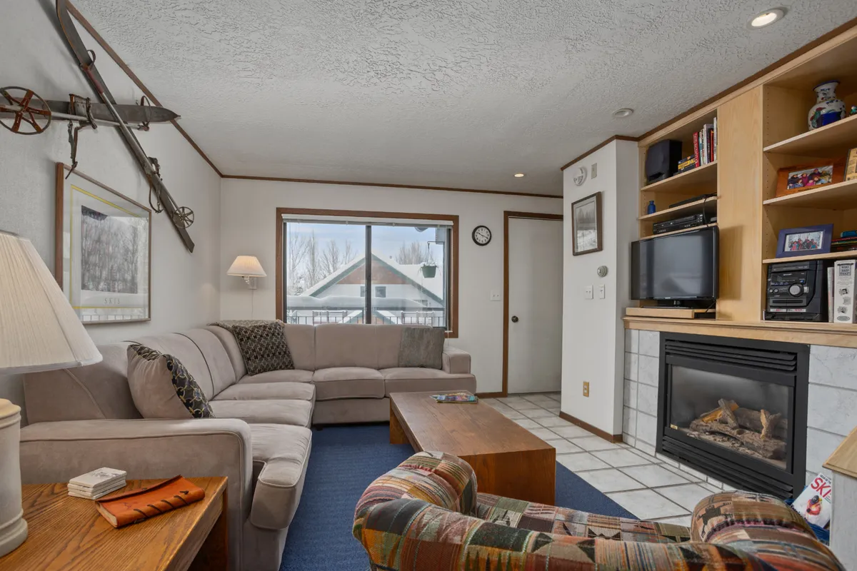 A cozy living room with a large, plush sofa arranged around a fireplace, complemented by a coffee table and a bookshelf. The room exudes warmth and is designed for socializing, relaxing, and unwinding after a day outdoors. Natural light fills the space, making it inviting for gatherings or quiet moments.