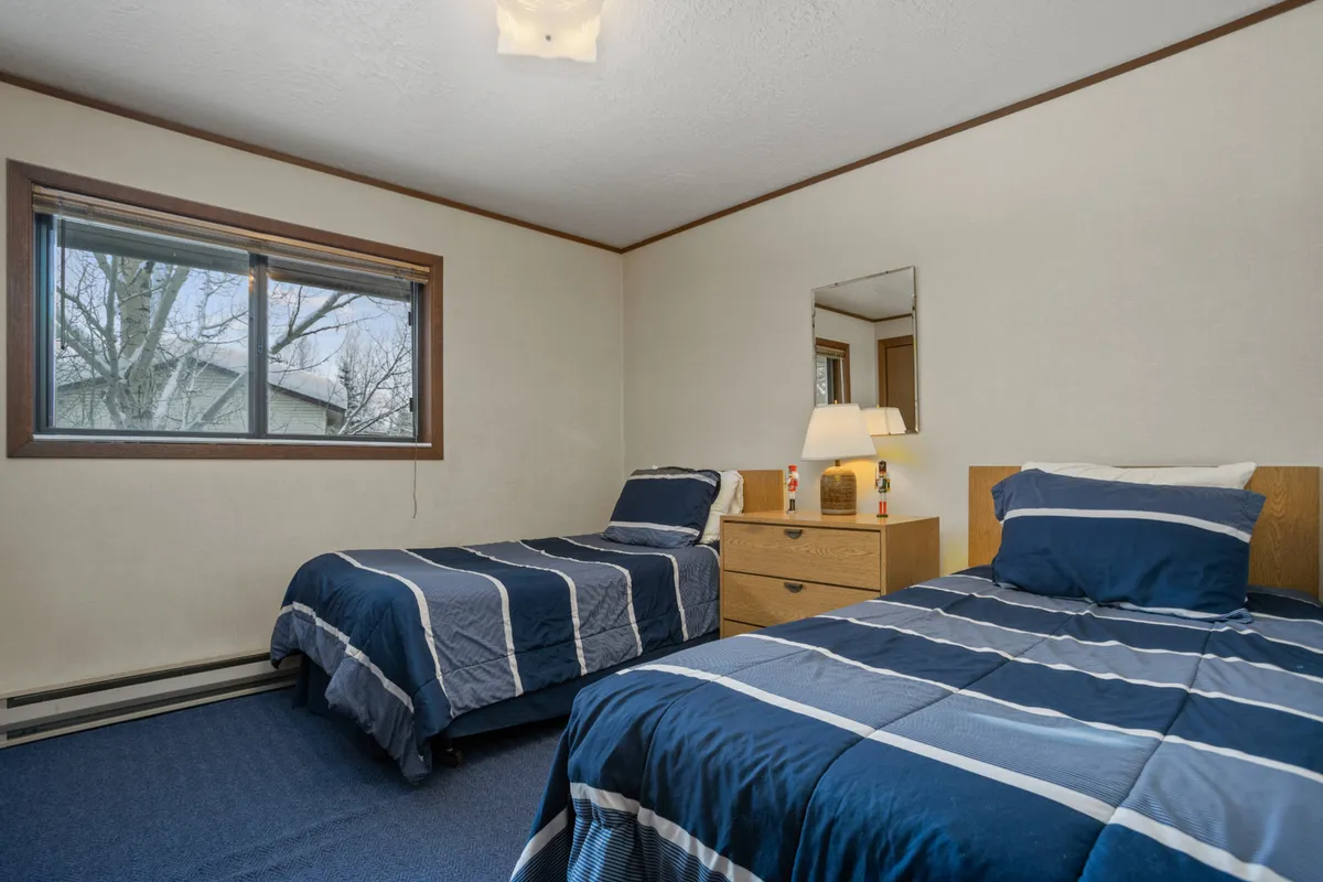 A cozy bedroom featuring two twin beds with a nightstand and lamp between them, plus a mirror on the wall. The layout is inviting and practical, supporting both relaxation and shared experiences for guests who may prefer not to share beds.