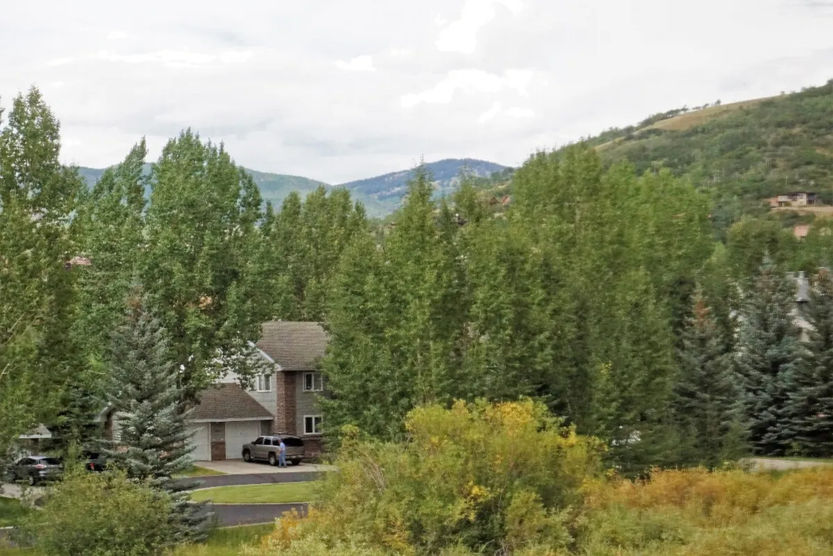 This image features a two-story house nestled among green trees, with a scenic mountain backdrop. The home sits comfortably in its natural surroundings, offering a sense of tranquility and access to outdoor adventures.