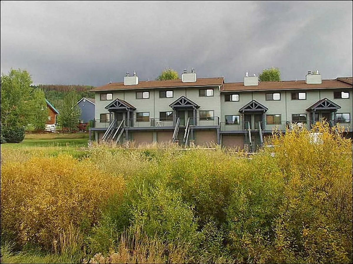 A tranquil townhouse structure surrounded by lush green foliage and yellow shrubbery, set beneath a dark sky. The inviting balconies and garden spaces suggest opportunities for enjoying the outdoors right at home.